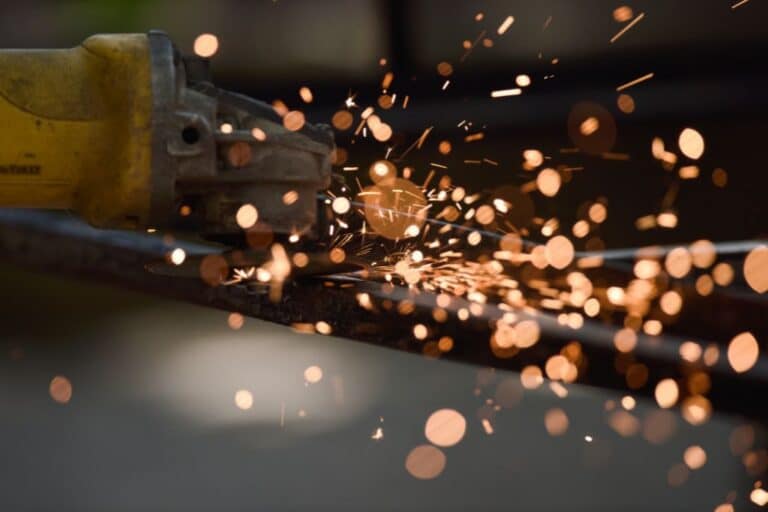 En närbild av en gul kraftslip som skär genom metall och skapar en spray av ljusa orange gnistor mot en suddig bakgrund.